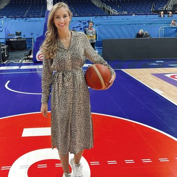 Frau mit Basketball auf dem Spielfeld in einem Leopardenkleid.