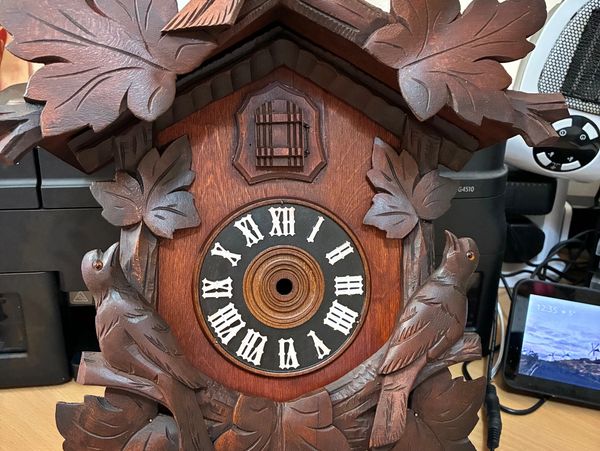 Wooden cuckoo clock with bird carvings and Roman numerals.