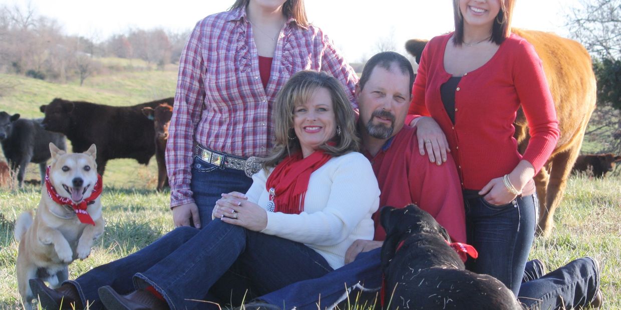 Happy family portrait outdoors with dogs and cows in the background.
