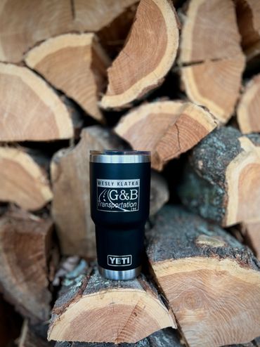 Black Yeti Rambler with custom engraved design of Company Logo and Name against wood logs background