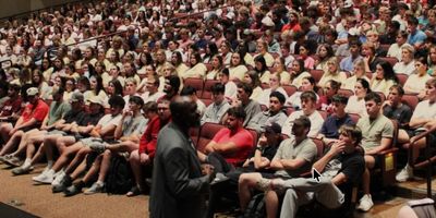 A crowded lecture hall filled with attentive students and a speaker at the front.