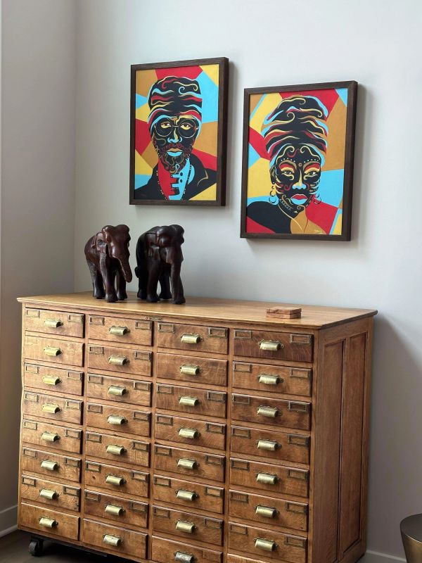 Wooden cabinet with brass handles, elephant sculptures, and colorful African-inspired portraits on the wall.