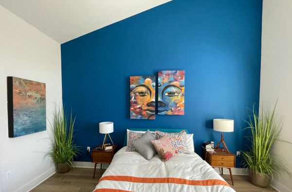 Modern bedroom with a blue accent wall and colorful artwork above the bed.