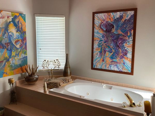 A modern bathroom with a large bathtub and colorful abstract paintings.