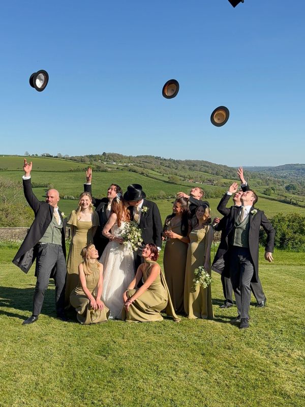Wedding party celebrates outdoors by tossing hats into the air.