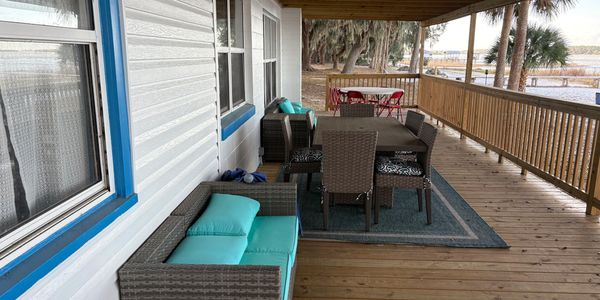 Cozy porch with wicker furniture and a wooden railing overlooking a scenic water view.