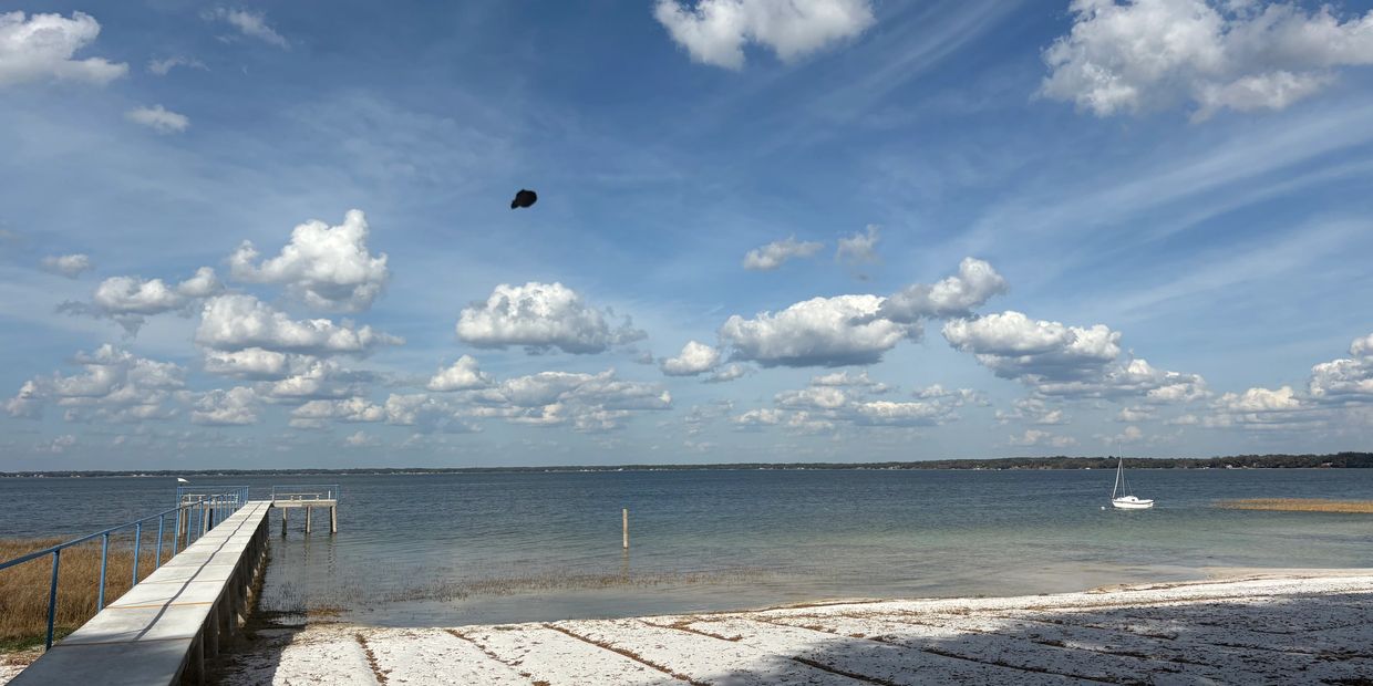 A pier extends over calm lake waters under a blue sky with scattered clouds.
