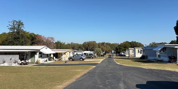Quiet suburban street with houses and parked cars under a clear blue sky.