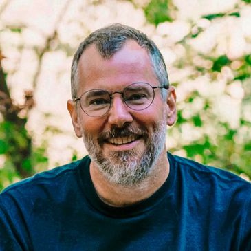 Smiling man with glasses and beard outdoors in natural light.