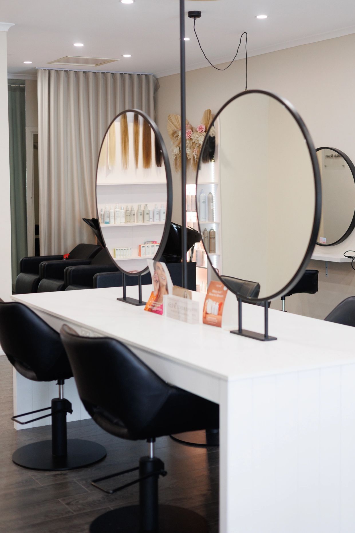 Modern hair salon with black chairs and round mirrors on a white counter.