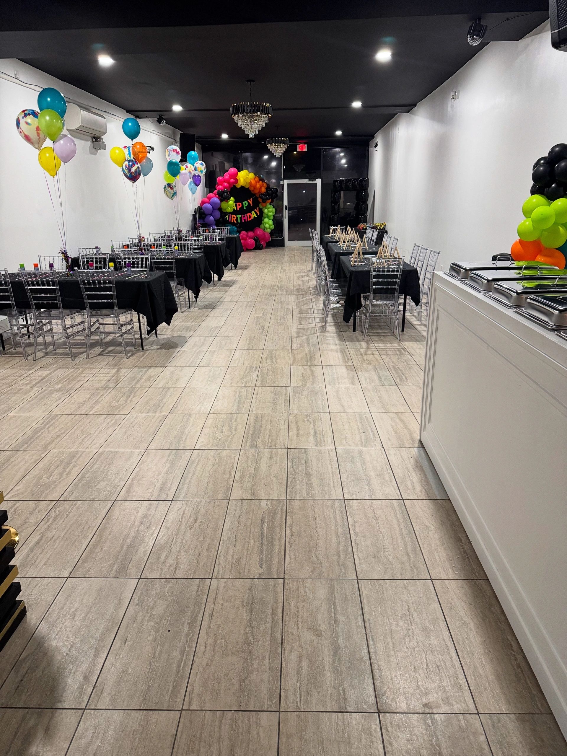 Long room set up for a colorful birthday party with balloons and tables.