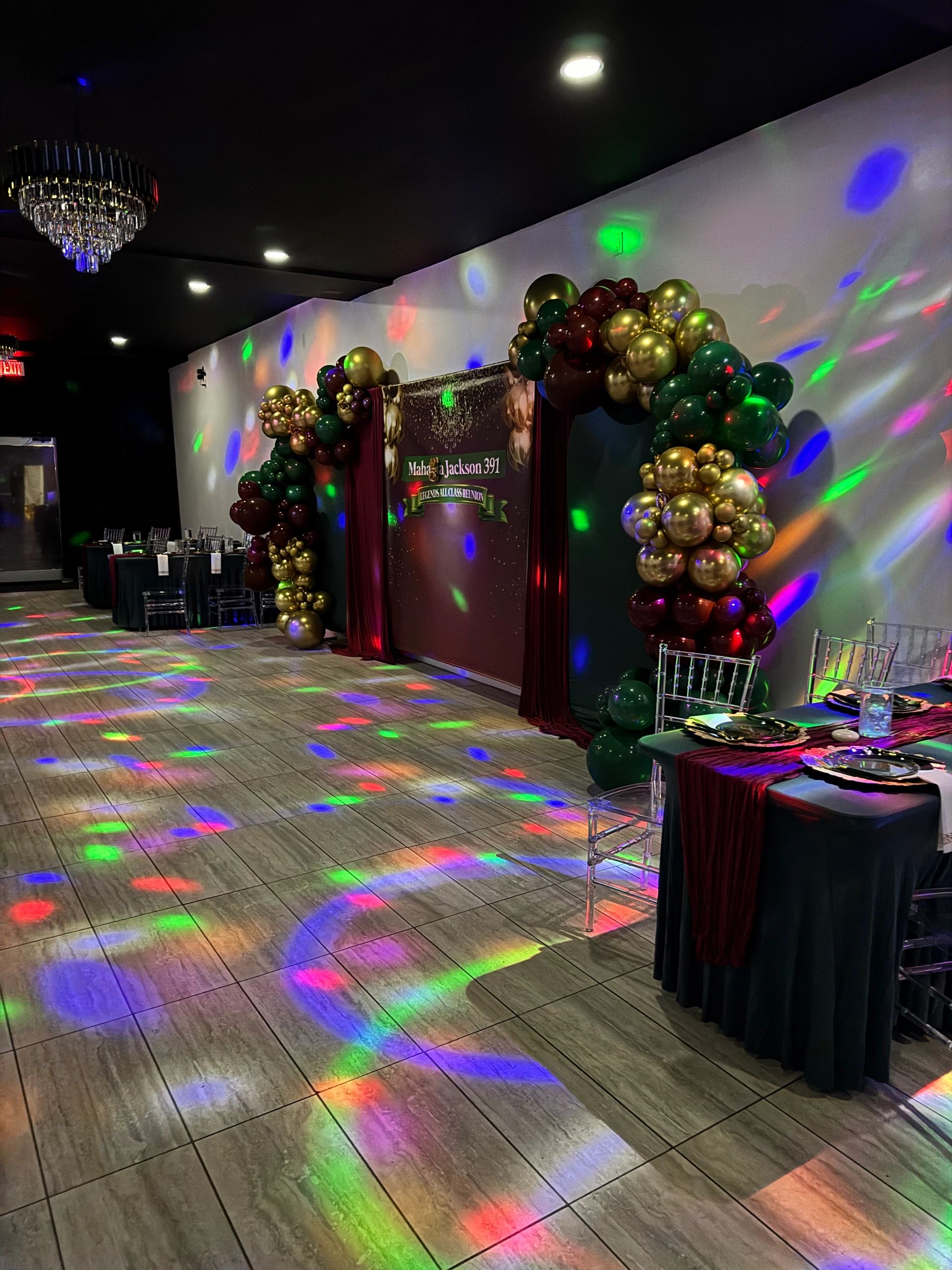 Event hall decorated with golden and green balloon arch and colorful lights.