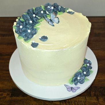 Elegant white cake decorated with blue flowers and butterflies.