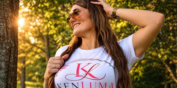 Young woman smiling outdoors wearing sunglasses and a white shirt.