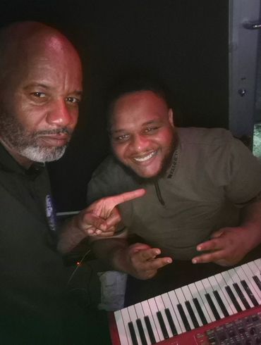 Two men smiling and posing by a keyboard in a dark room.