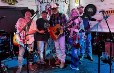 Band posing on stage with instruments in vibrant lighting.