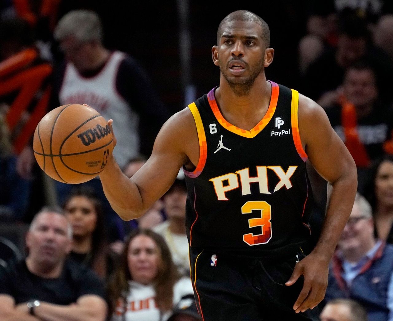 Chris Paul, wearing a black 'PHX' jersey, dribbles a basketball while focusing on the game during a match.