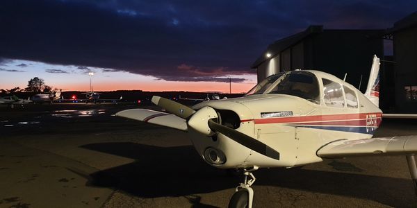 Small airplane parked on runway during twilight with dramatic sky.
