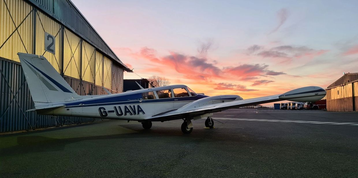 Twin Comanche plane next to hangar at sunset