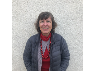 Smiling woman in a jacket standing against a textured wall.