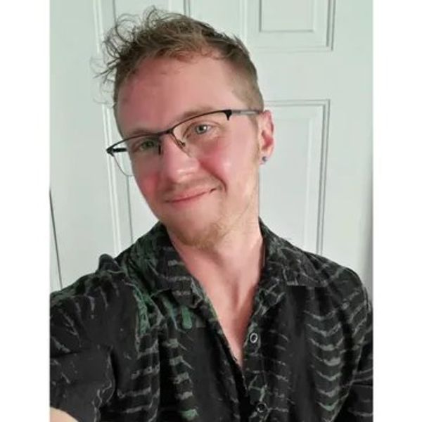 Young man with glasses smiling, wearing a patterned black shirt.
