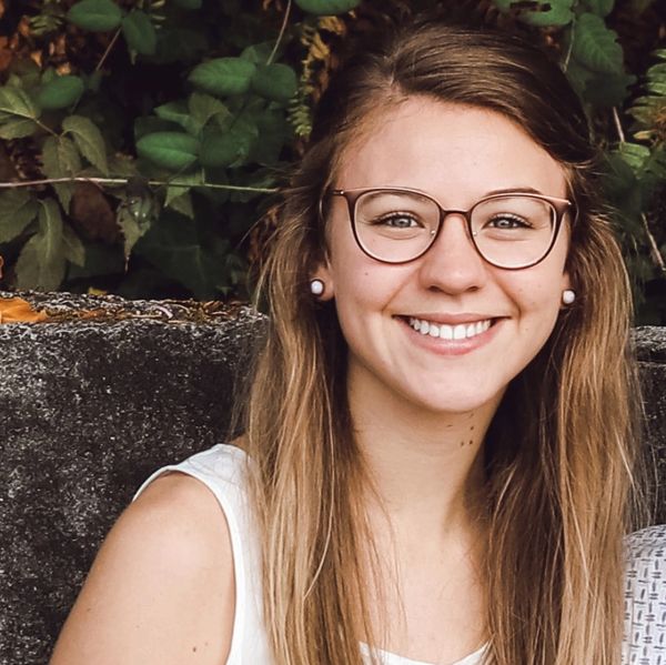 Smiling woman with glasses and long hair outdoors.