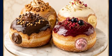 Four assorted gourmet donuts on a marble plate.