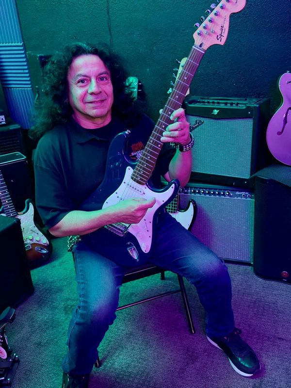 Man with long hair playing electric guitar in a music room.