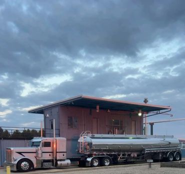 A shiny tanker truck parked near an industrial building under a cloudy sky.