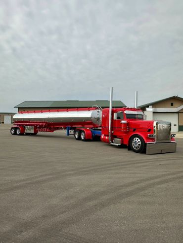 A shiny red semi-truck with a silver tanker trailer parked on a paved surface.