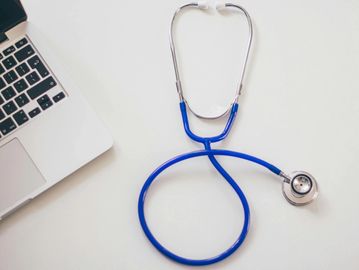 Blue stethoscope next to a laptop on a white surface.
