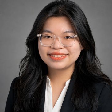 Professional portrait of a young woman with glasses and long black hair.