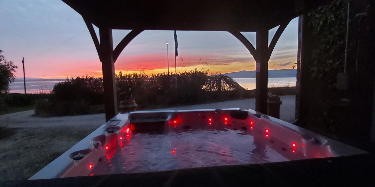 Hot tub glowing red under a covered patio at sunset by the water.