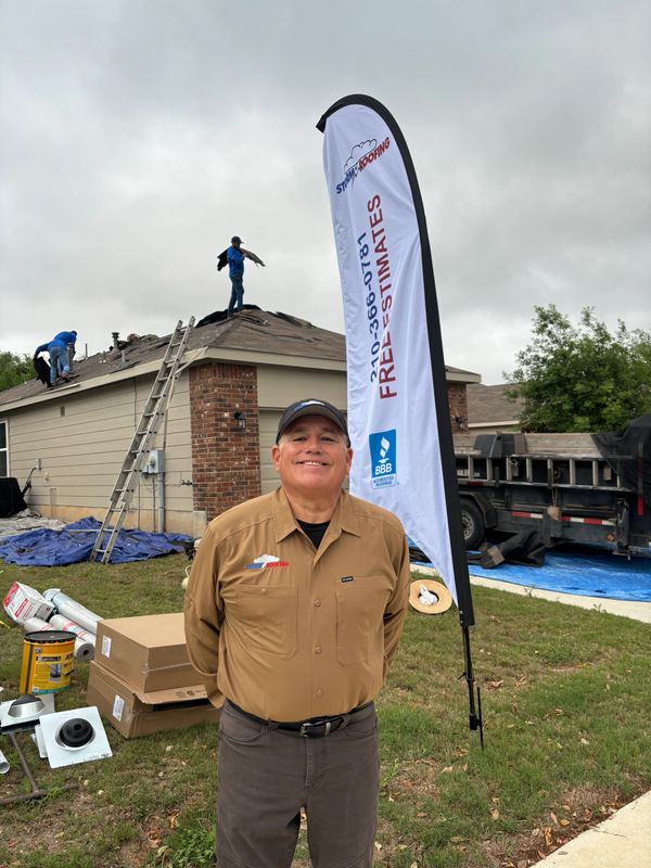 Man smiling in front of a house under roofing repair with a promotional flag.