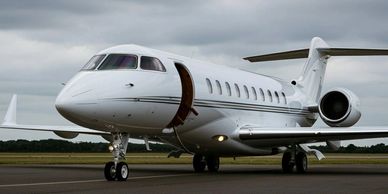 A white private jet with door open on a runway under cloudy sky.
