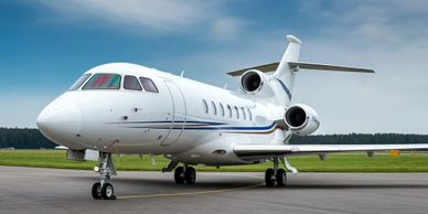 A sleek white private jet parked on an airport runway under a partly cloudy sky.