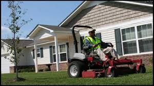 Person mowing lawn with riding mower in front of house.