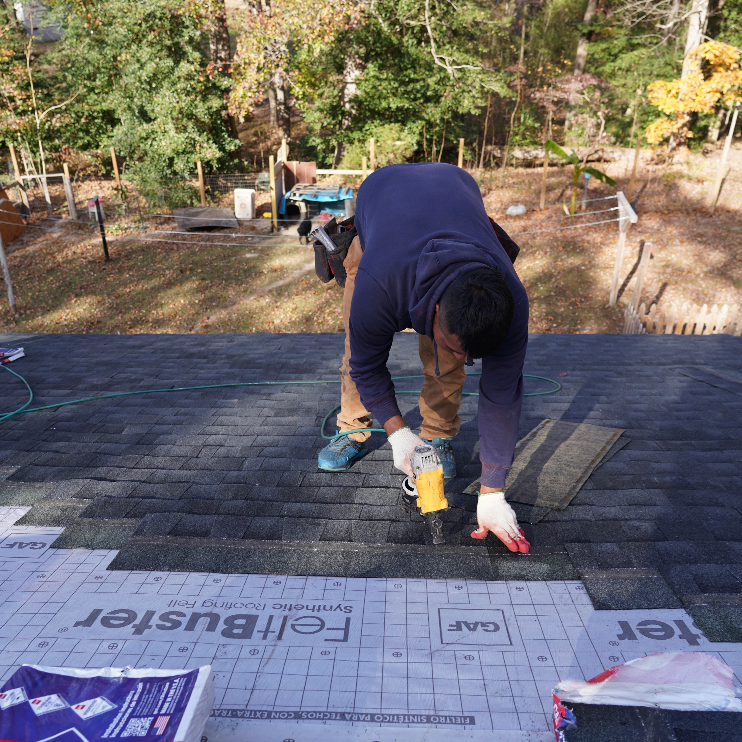 A man installing shingles on a roof using a nail gun.