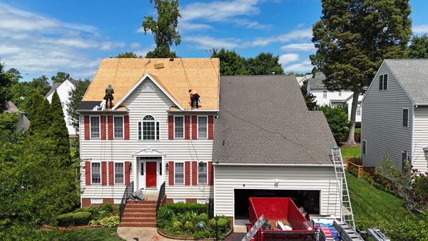 Workers replace roof on a suburban house under clear blue sky.