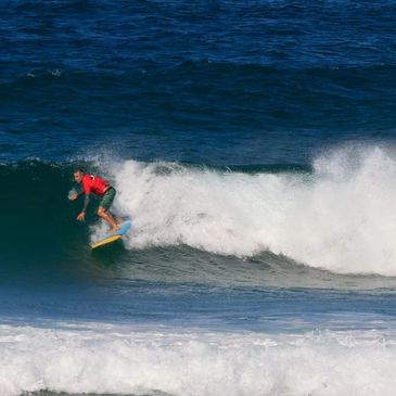 Surfer in a red shirt riding a wave on a yellow surfboard.