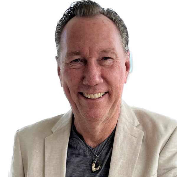 Smiling man in beige blazer and necklace.