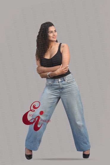 Woman with curly hair wearing black top and wide-leg jeans posing confidently.
