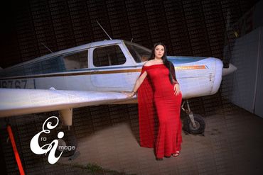 Woman in a red dress poses beside a small white airplane inside a hangar.
