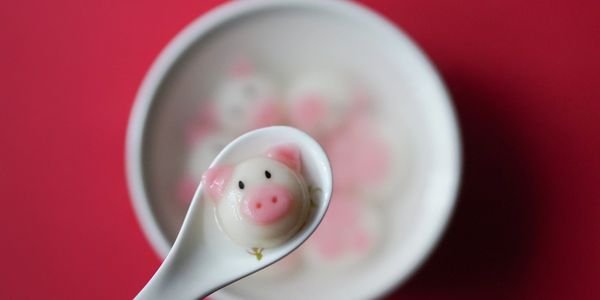 Cute pink pig face on a ceramic spoon, surrounded by other pink pigs, immersed in a ceramic bowl.