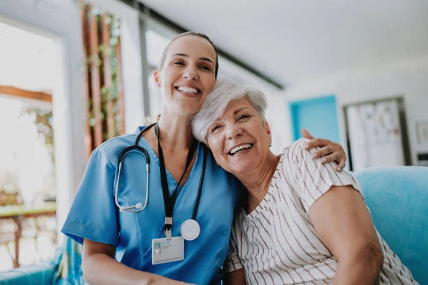 A smiling nurse embraces an elderly woman in a warm, caring moment.