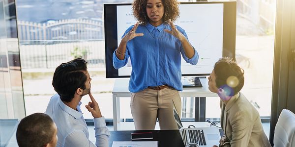 A woman presenting to colleagues in a modern office meeting.