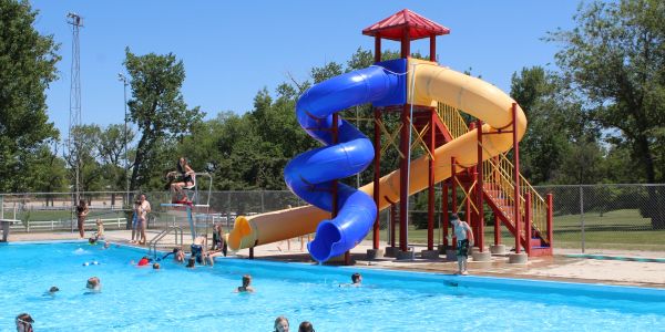 Outdoor pool with water slides and people swimming.