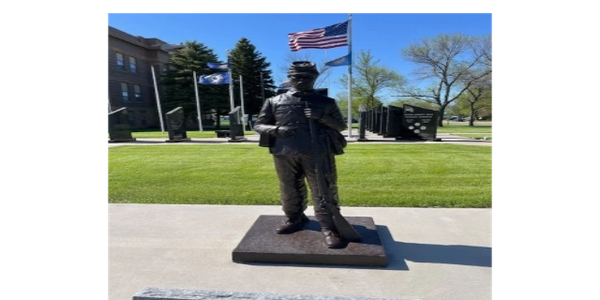 Statue of a soldier holding a rifle outdoors with flags in the background.