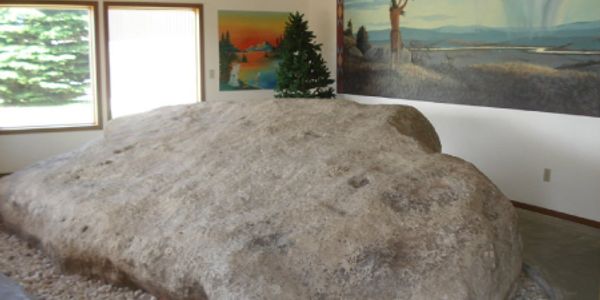 Large rock inside a room near windows and paintings.