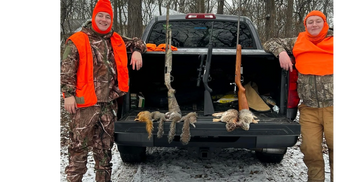 Two hunters in orange gear stand by a truck with hunted squirrels and rifles displayed.